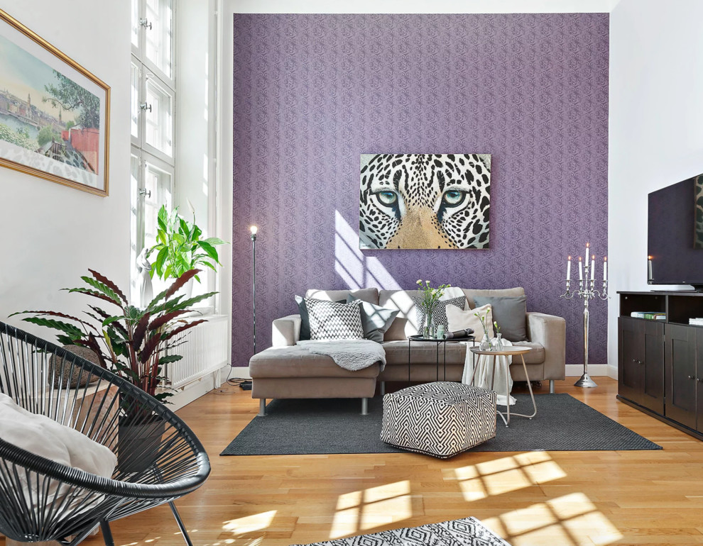 Eclectic grey and purple living room feature wall in Stockholm with medium hardwood flooring, purple walls, a freestanding tv and beige floors.