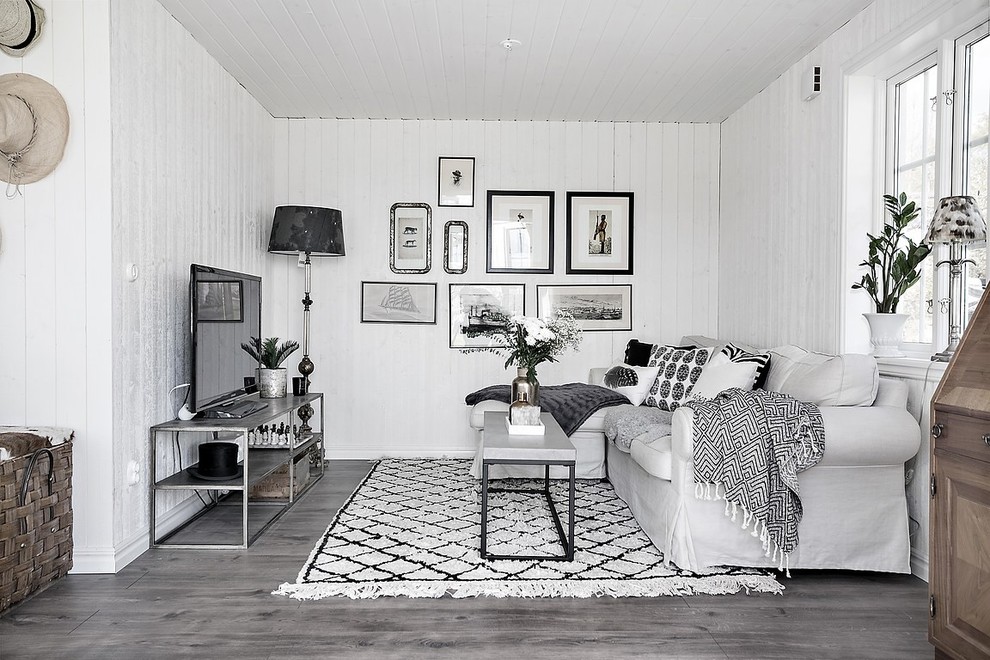 Inredning av ett skandinaviskt vardagsrum, med vita väggar, mellanmörkt trägolv, en fristående TV och grått golv