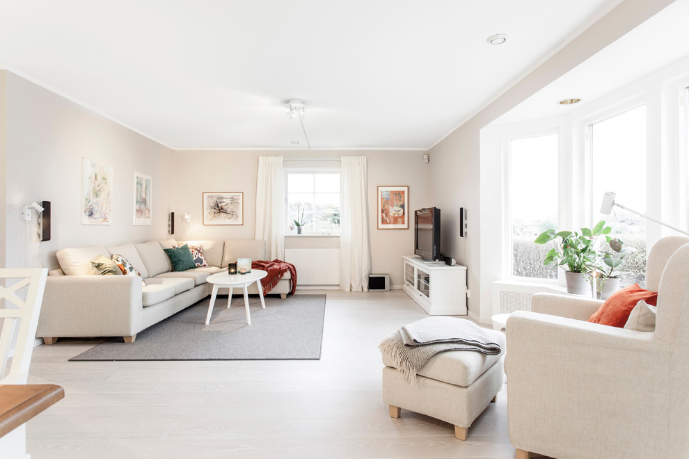 Offenes, Großes Skandinavisches Wohnzimmer ohne Kamin mit freistehendem TV, beiger Wandfarbe und hellem Holzboden in Göteborg