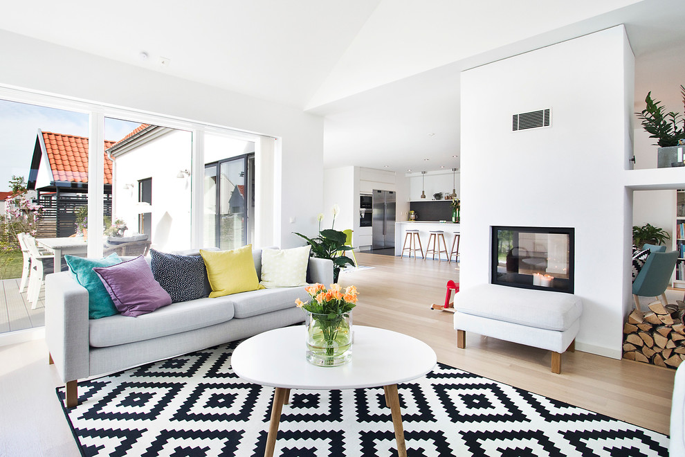 Cette image montre un grand salon nordique ouvert avec une salle de réception, un mur blanc, une cheminée double-face, parquet clair et aucun téléviseur.