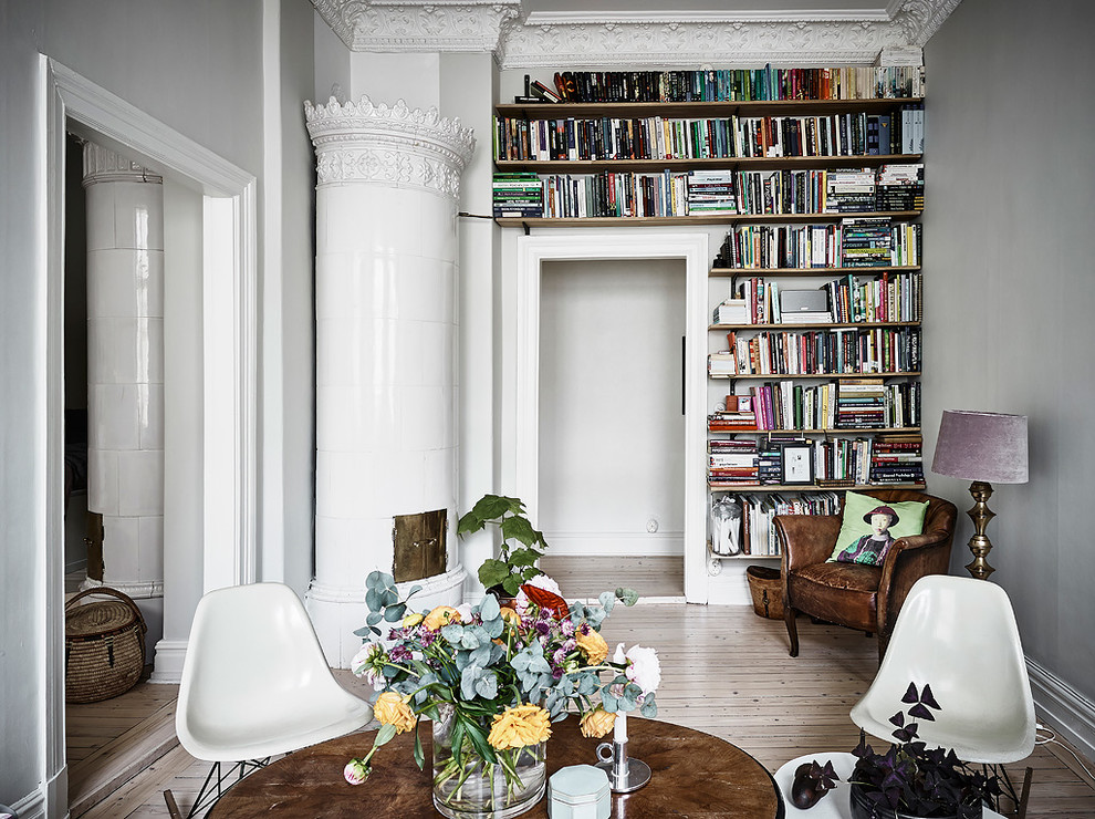 Imagen de biblioteca en casa cerrada escandinava sin televisor con paredes grises, suelo de madera clara, chimenea de esquina, marco de chimenea de metal y suelo beige