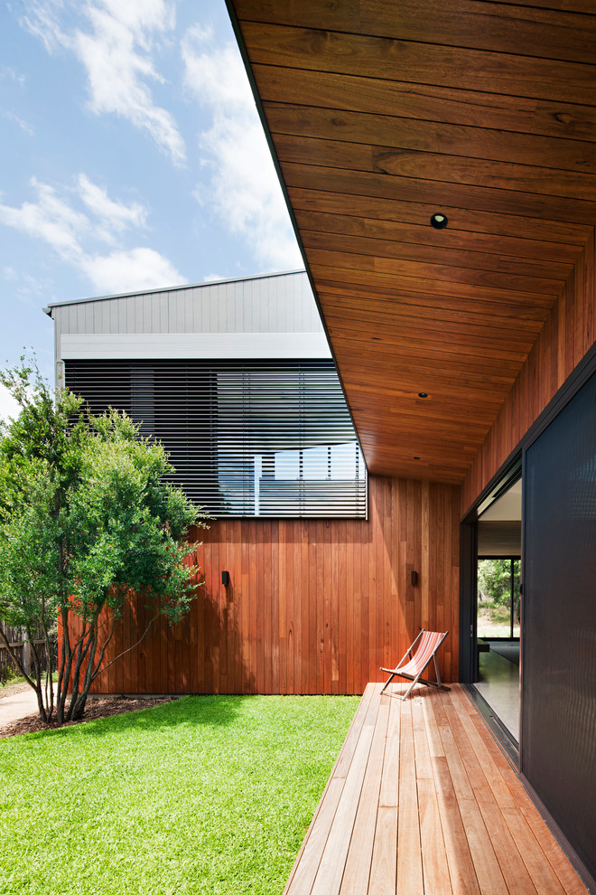Réalisation d'un porche d'entrée de maison design avec une terrasse en bois et une extension de toiture.