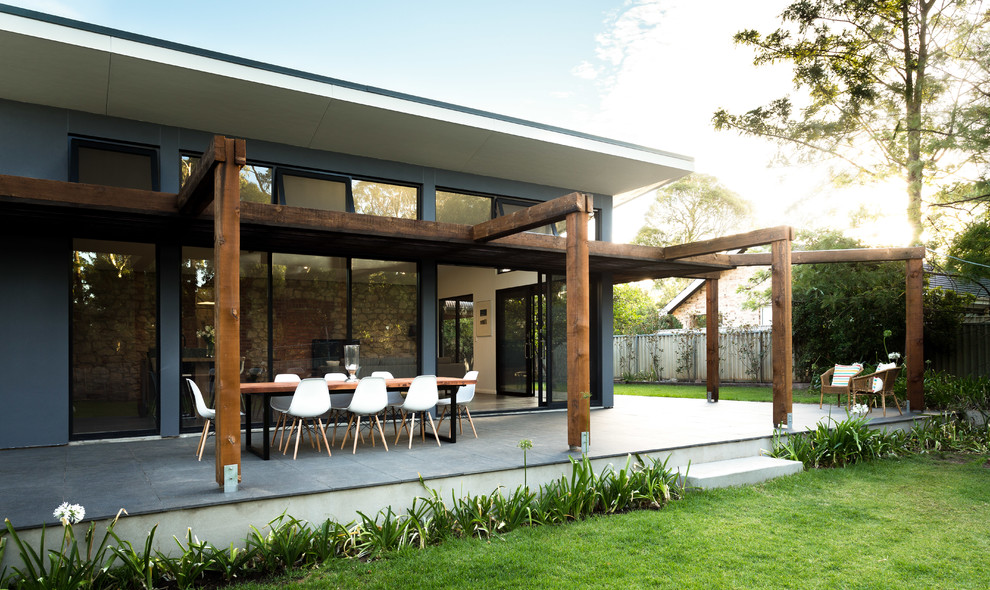 Cette image montre un grand porche d'entrée de maison arrière design avec du carrelage et une pergola.