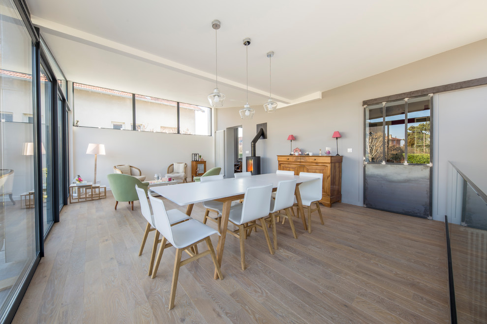 Cette image montre une grande salle à manger design avec parquet clair, un poêle à bois, un manteau de cheminée en carrelage et un sol beige.