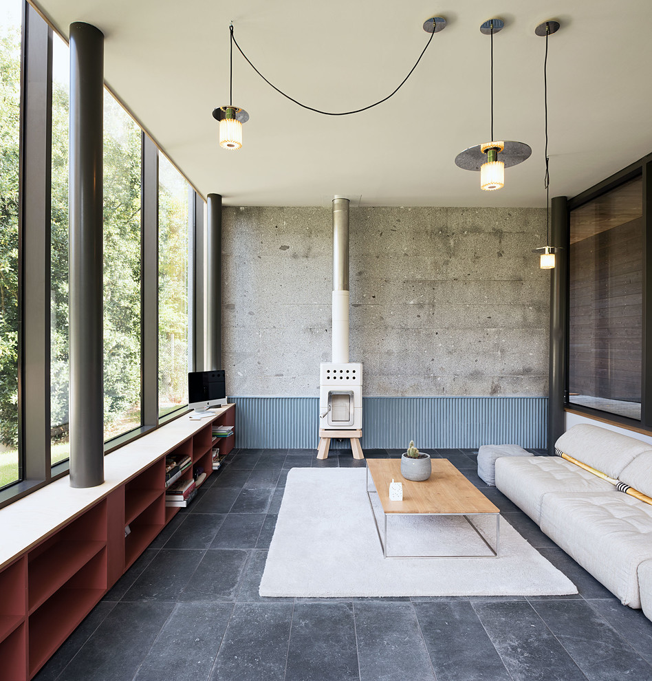 Идея дизайна: открытая гостиная комната среднего размера в стиле лофт с серыми стенами, полом из керамической плитки, печью-буржуйкой, фасадом камина из каменной кладки, телевизором в углу, серым полом и кирпичными стенами