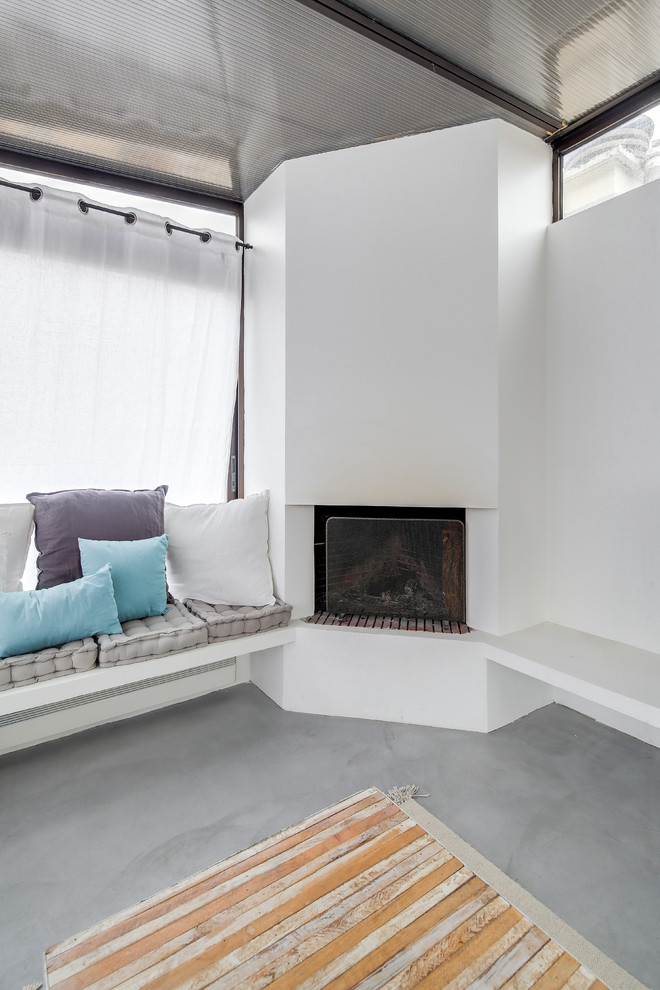 Aménagement d'une grande véranda contemporaine avec sol en béton ciré, une cheminée d'angle, un manteau de cheminée en plâtre, un plafond standard et un sol gris.