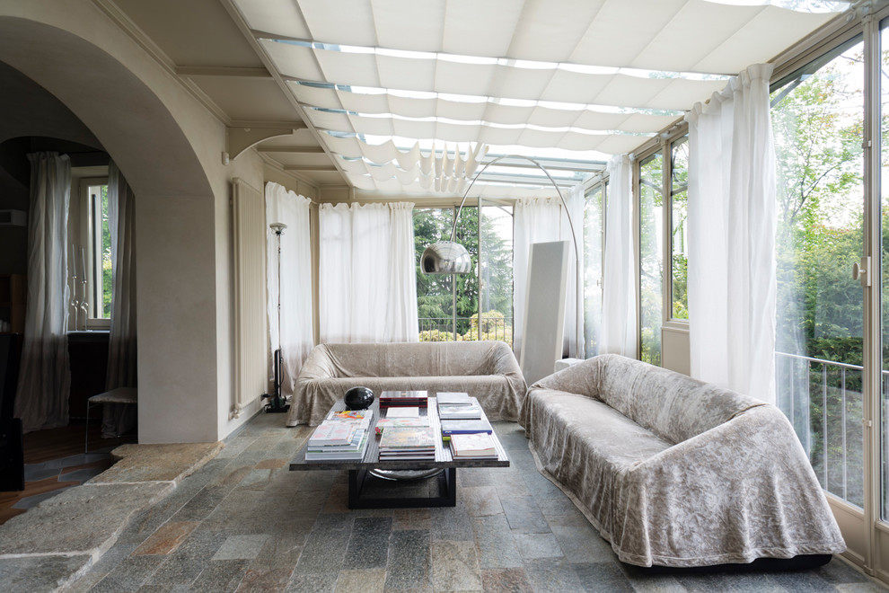 Cette image montre une grande véranda design avec un sol en calcaire, un plafond en verre et un sol gris.