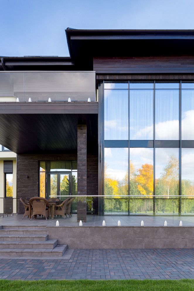 Foto på en stor nordisk veranda på baksidan av huset, med utekök, naturstensplattor, markiser och räcke i glas