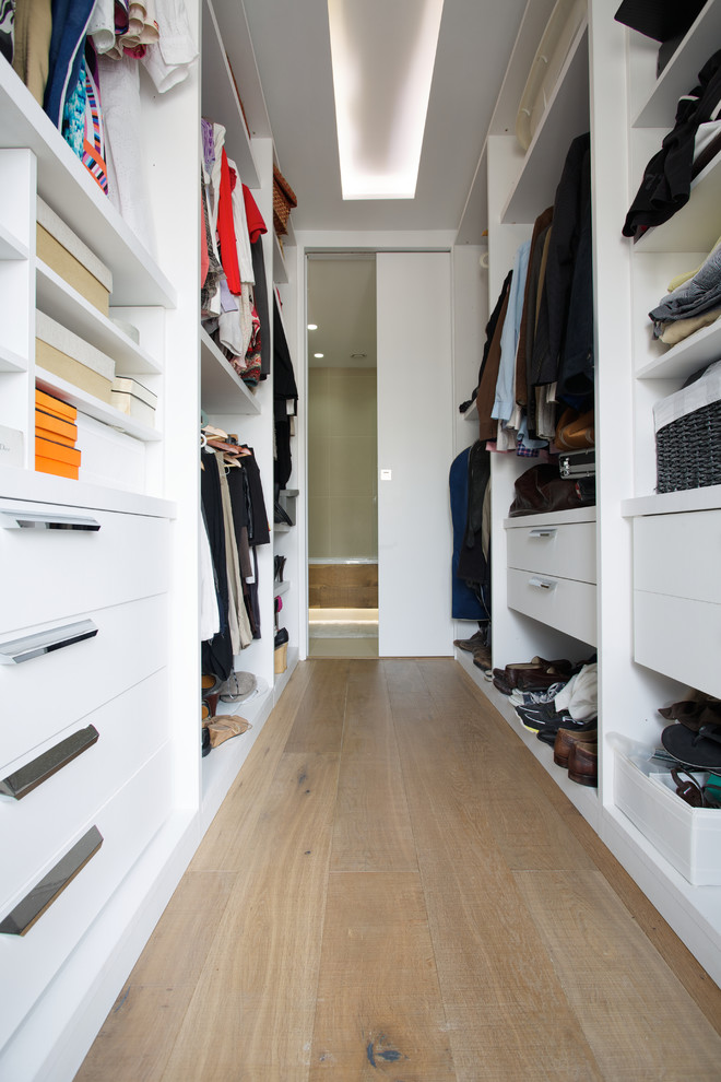 Diseño de armario y vestidor unisex actual con armarios con paneles lisos, puertas de armario blancas y suelo de madera en tonos medios