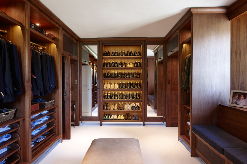 Large classic dressing room for men in London with open cabinets, dark wood cabinets, carpet and white floors.