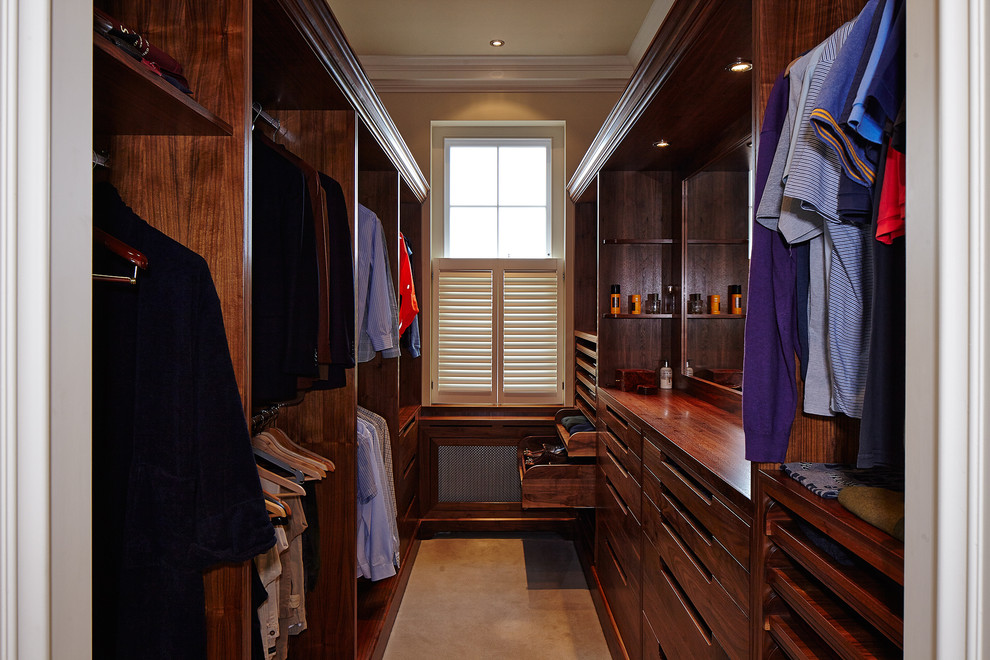 На фото: гардеробная комната унисекс в классическом стиле с темными деревянными фасадами и коричневым полом с