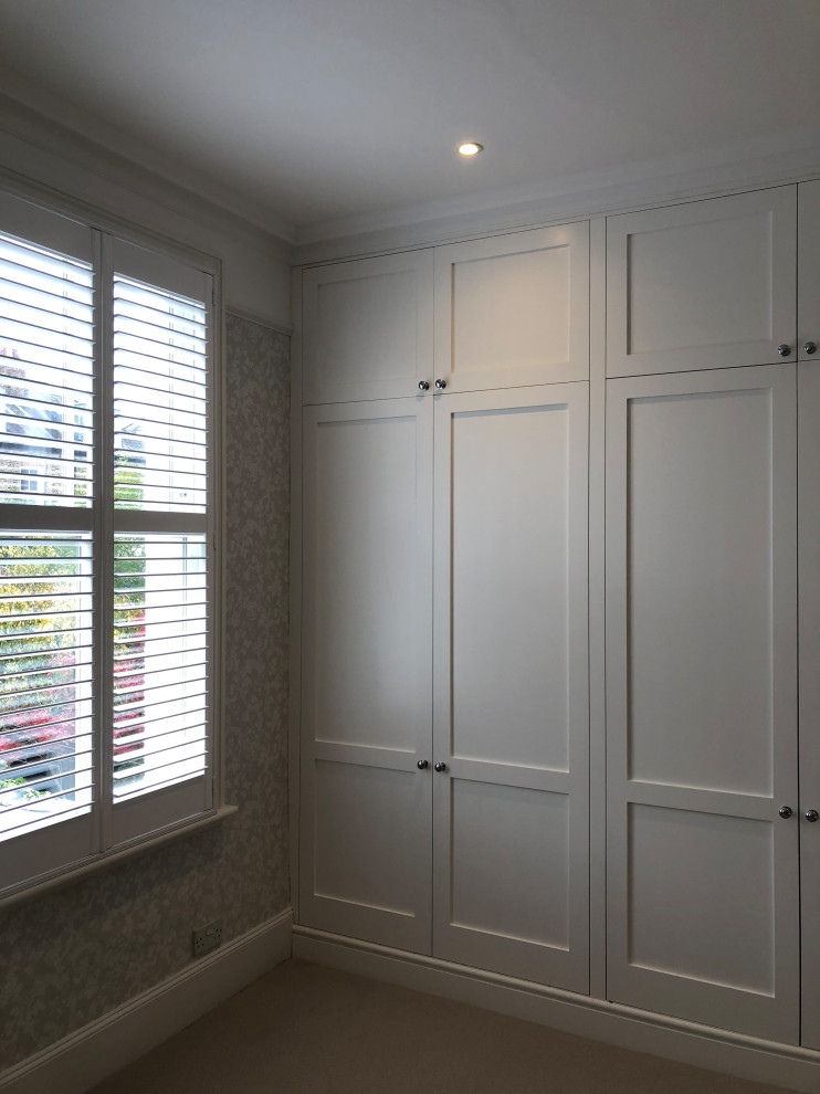 Expansive victorian built-in wardrobe in London with recessed-panel cabinets, white cabinets, carpet and beige floors.