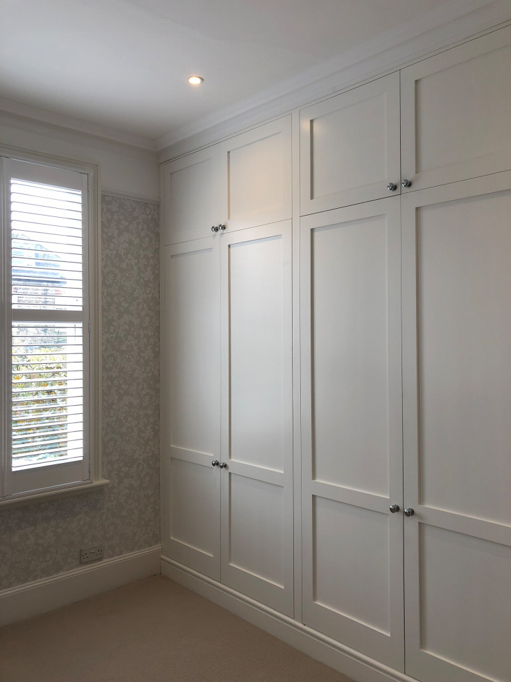 Cette image montre une très grande armoire encastrée victorienne avec un placard avec porte à panneau encastré, des portes de placard blanches, moquette et un sol beige.