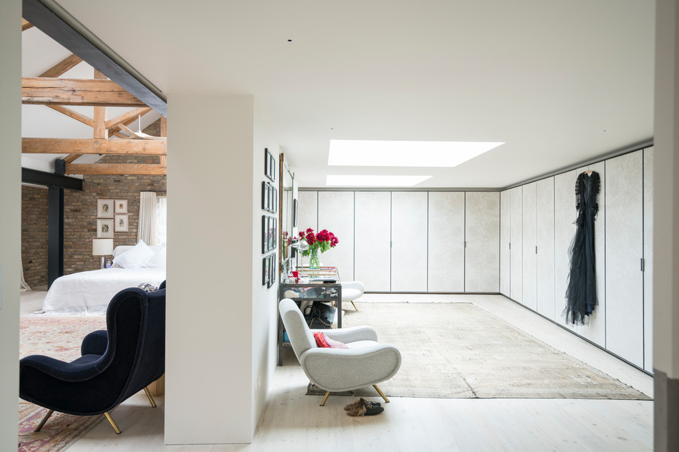 Walk-in closet - large industrial women's light wood floor and white floor walk-in closet idea in London with flat-panel cabinets and white cabinets