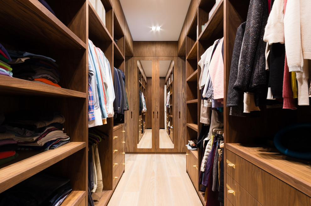 Imagen de vestidor unisex actual de tamaño medio con armarios con paneles lisos, puertas de armario de madera oscura y suelo de madera clara