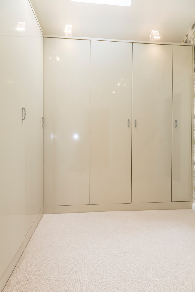 Großes Modernes Ankleidezimmer mit Ankleidebereich, flächenbündigen Schrankfronten, beigen Schränken, Teppichboden und beigem Boden in Dorset