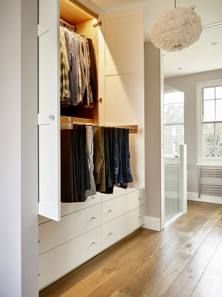 Modelo de vestidor unisex contemporáneo de tamaño medio con armarios estilo shaker, puertas de armario blancas y suelo de madera en tonos medios
