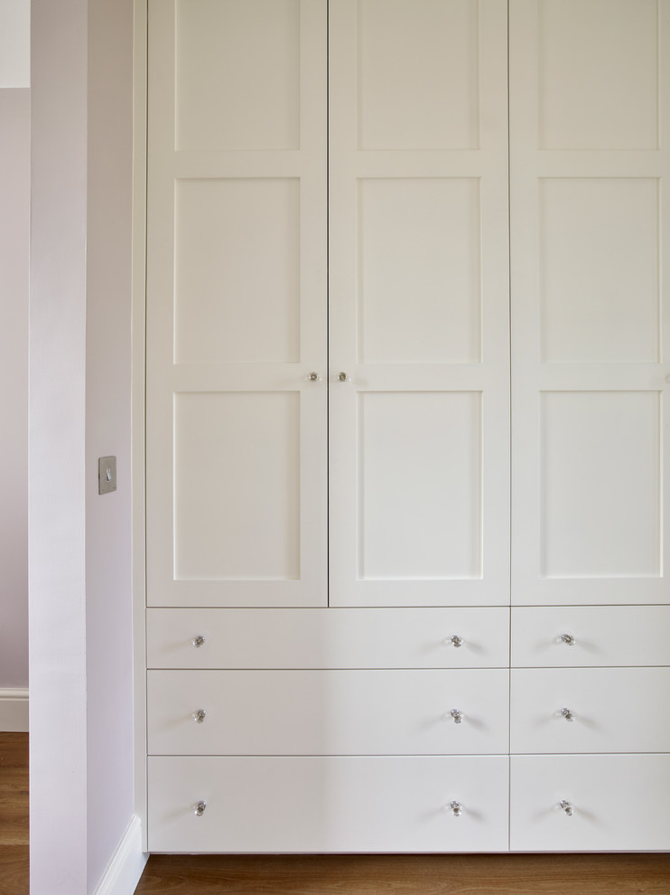 Exemple d'un dressing room tendance de taille moyenne et neutre avec un placard à porte shaker, des portes de placard blanches et un sol en bois brun.