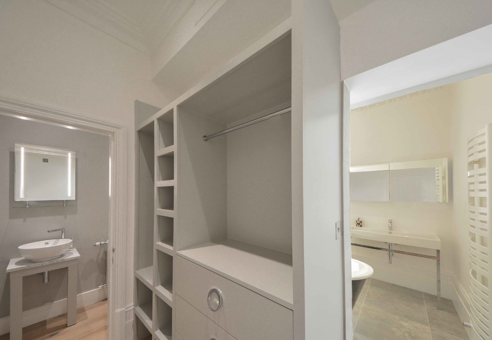 Small contemporary gender neutral dressing room in Kent with open cabinets, grey cabinets and light hardwood flooring.