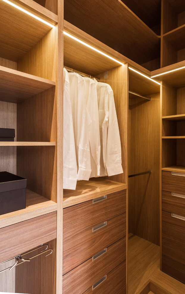 Diseño de armario vestidor unisex actual de tamaño medio con armarios con paneles lisos, puertas de armario de madera oscura, suelo de madera en tonos medios y suelo beige