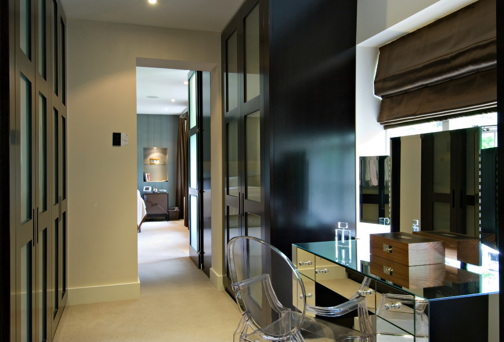 Photo of a medium sized traditional gender neutral dressing room in London with glass-front cabinets, dark wood cabinets and carpet.