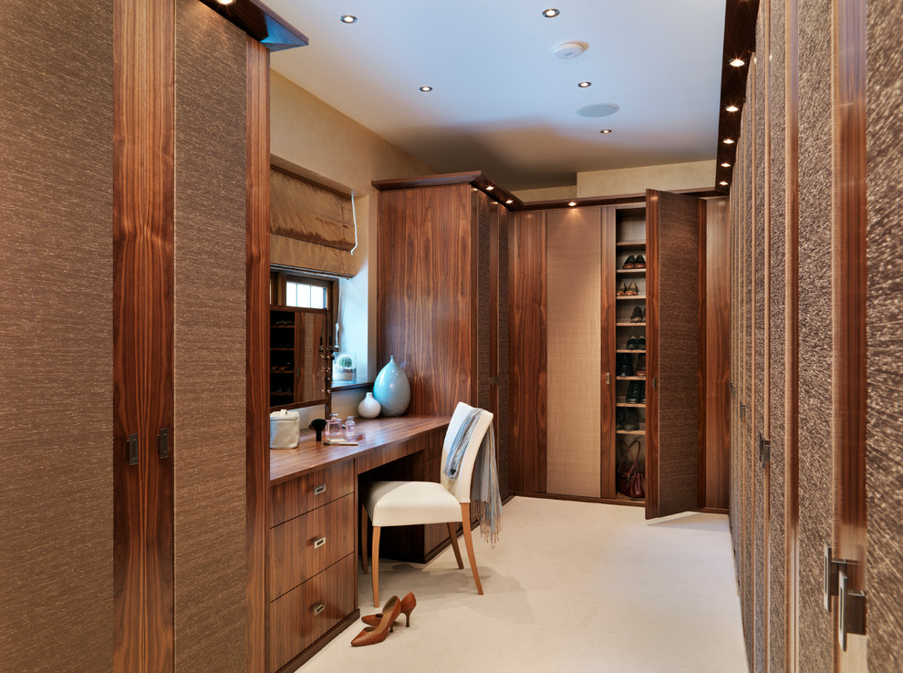 Large contemporary walk-in wardrobe in Cambridgeshire with carpet, flat-panel cabinets and dark wood cabinets.
