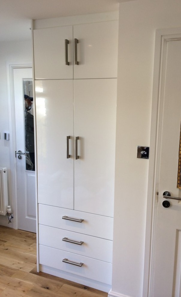 Foto de armario unisex moderno pequeño con armarios con paneles lisos, puertas de armario blancas y suelo de madera clara