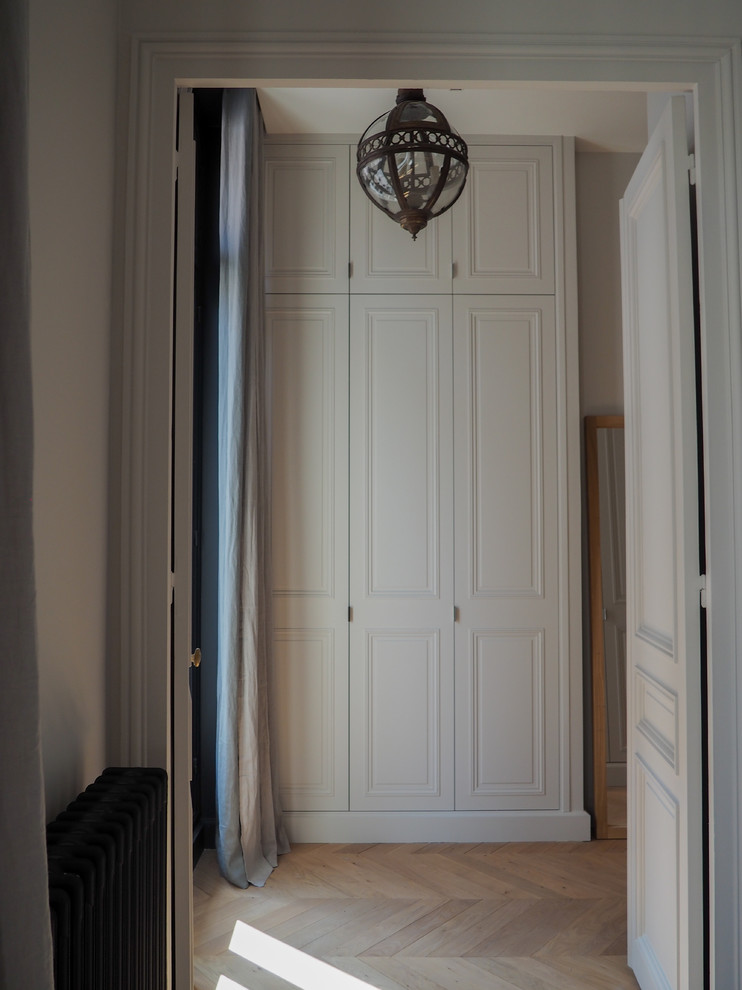 Exemple d'un dressing room tendance neutre avec des portes de placard blanches, parquet clair et un placard avec porte à panneau surélevé.