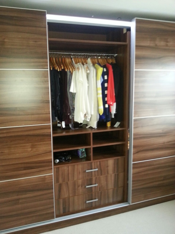 This is an example of a small gender neutral standard wardrobe in Other with medium wood cabinets and carpet.
