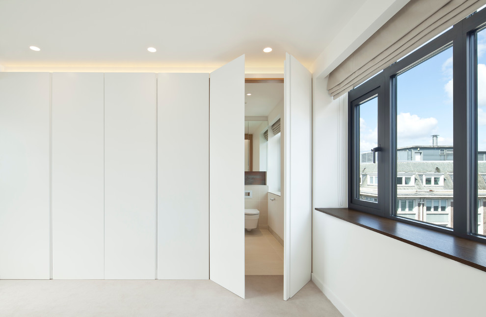 Inspiration for a modern gender neutral walk-in wardrobe in London with white cabinets, flat-panel cabinets and carpet.