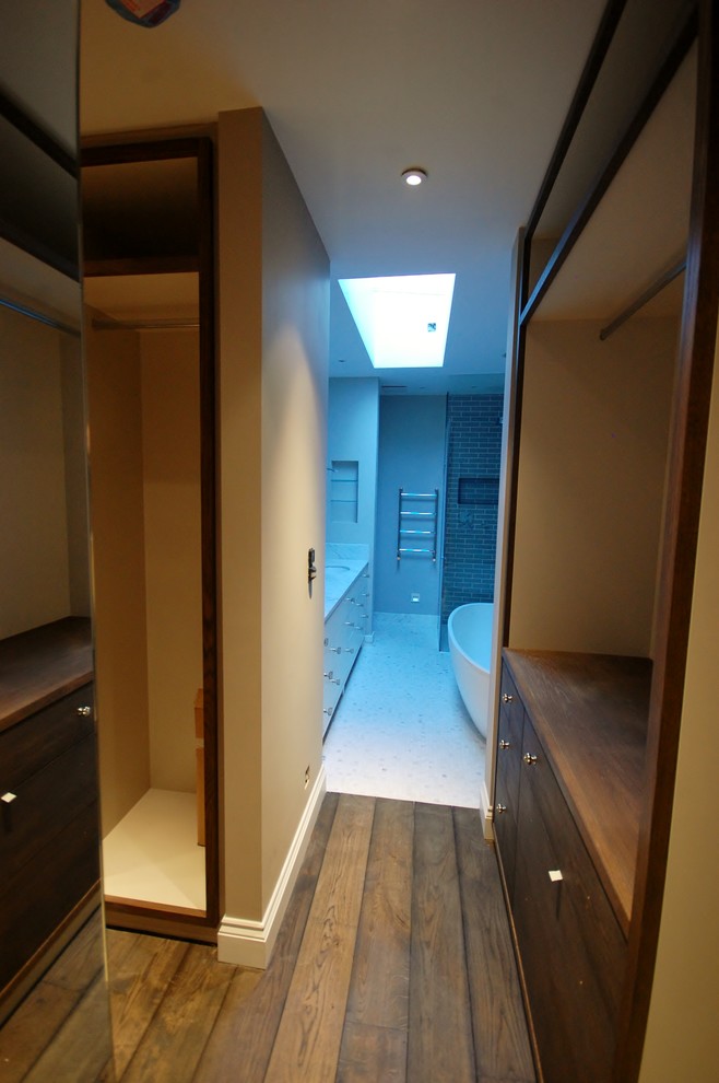 Modern inredning av ett mellanstort walk-in-closet för könsneutrala, med släta luckor, skåp i mörkt trä och mörkt trägolv