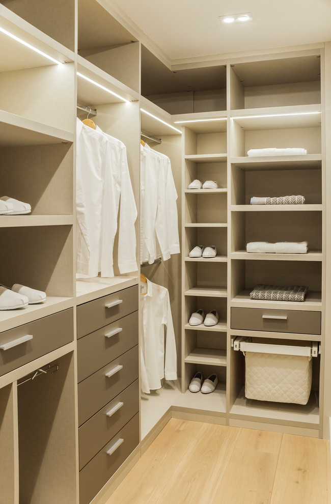 This is an example of a medium sized contemporary gender neutral walk-in wardrobe in London with open cabinets, brown cabinets, light hardwood flooring and beige floors.