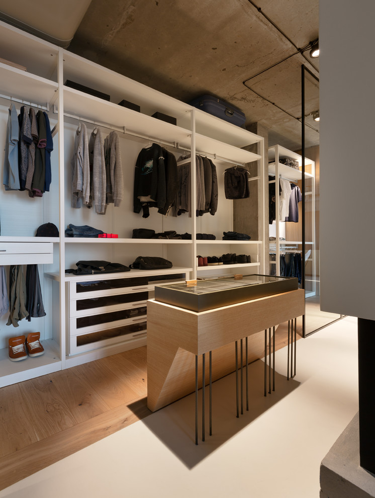 Ejemplo de armario vestidor de hombre industrial con armarios abiertos, puertas de armario blancas, suelo de madera en tonos medios y suelo marrón