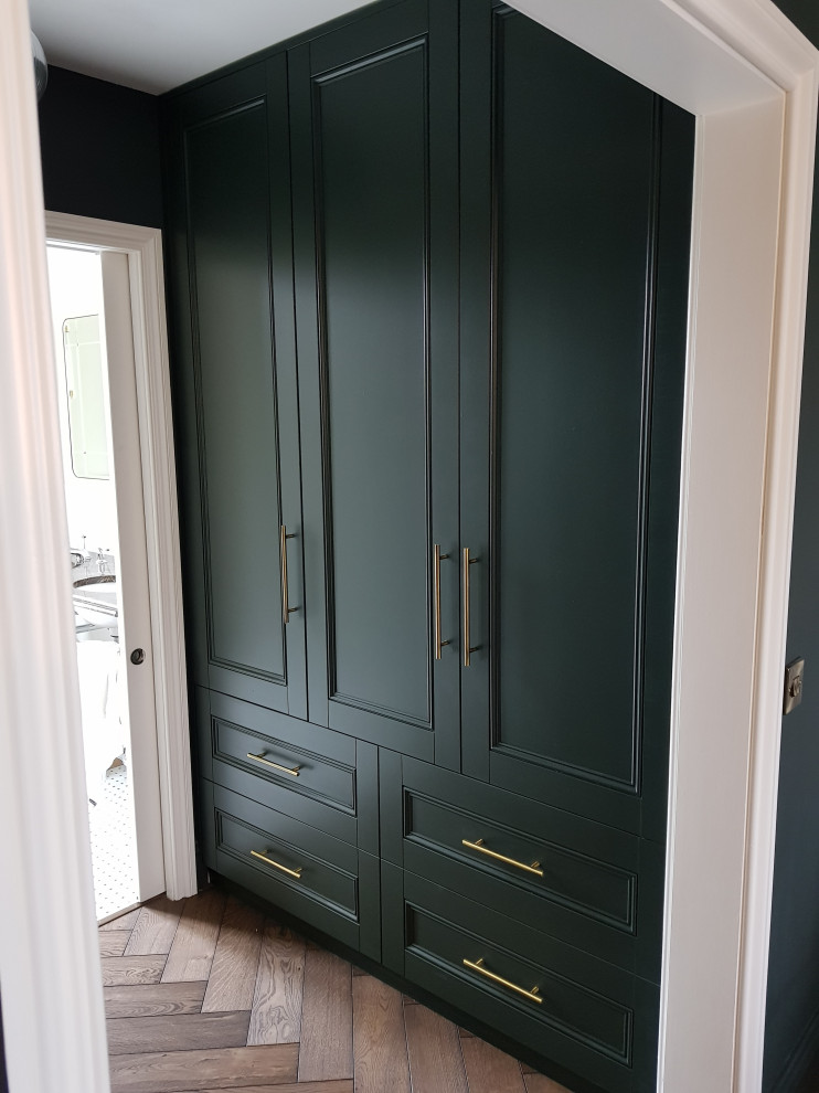 Ejemplo de vestidor unisex clásico de tamaño medio con armarios con paneles empotrados, puertas de armario verdes, suelo de madera en tonos medios y suelo marrón