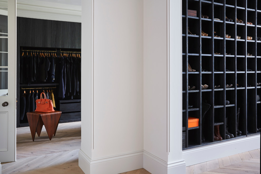 Large contemporary walk-in wardrobe in London with flat-panel cabinets, black cabinets and light hardwood flooring.