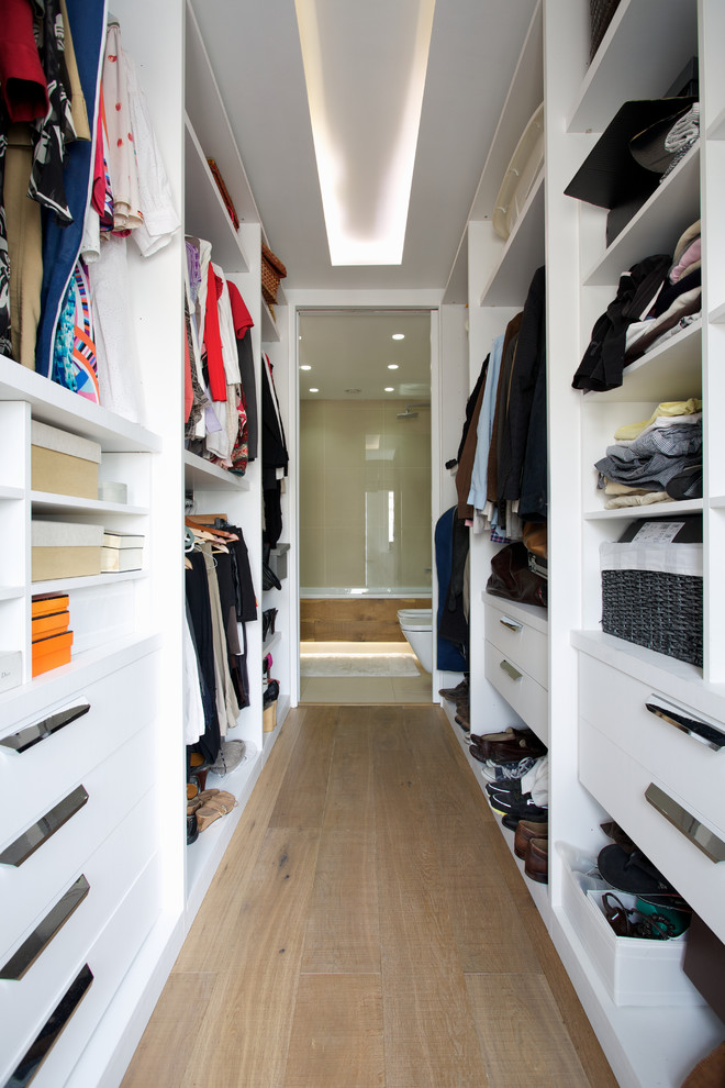 This is an example of a medium sized contemporary walk-in wardrobe in London with open cabinets, white cabinets and medium hardwood flooring.