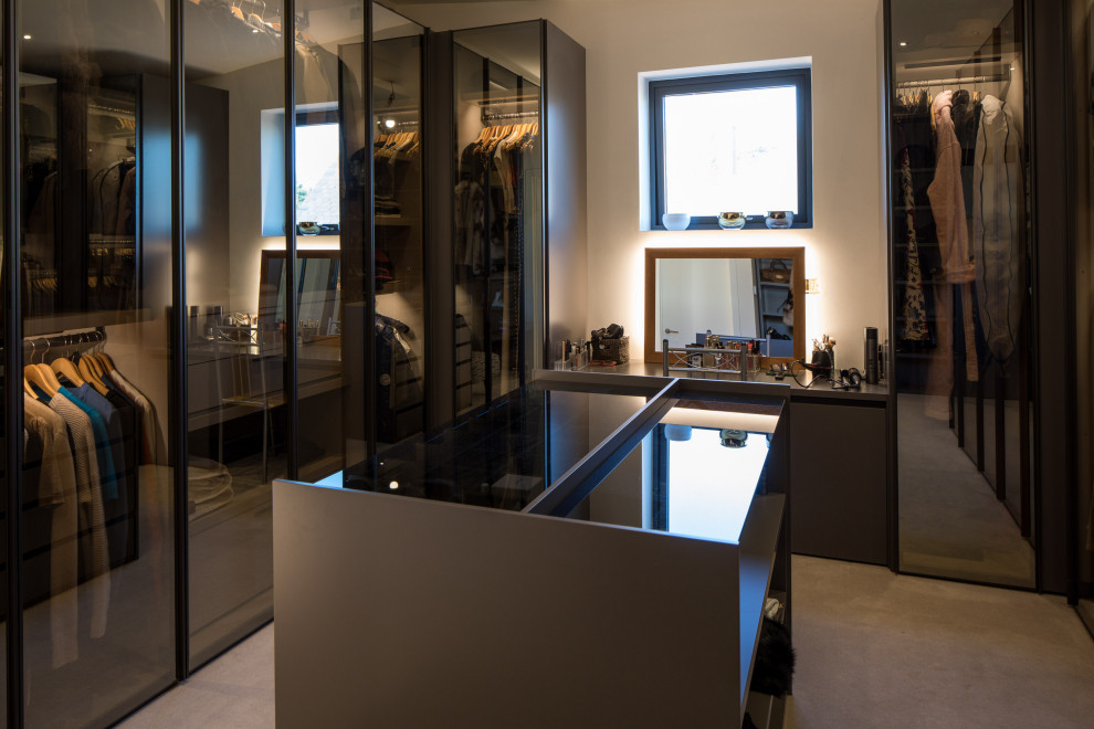 Photo of a medium sized modern gender neutral walk-in wardrobe in Devon with glass-front cabinets, grey cabinets, carpet, beige floors and feature lighting.