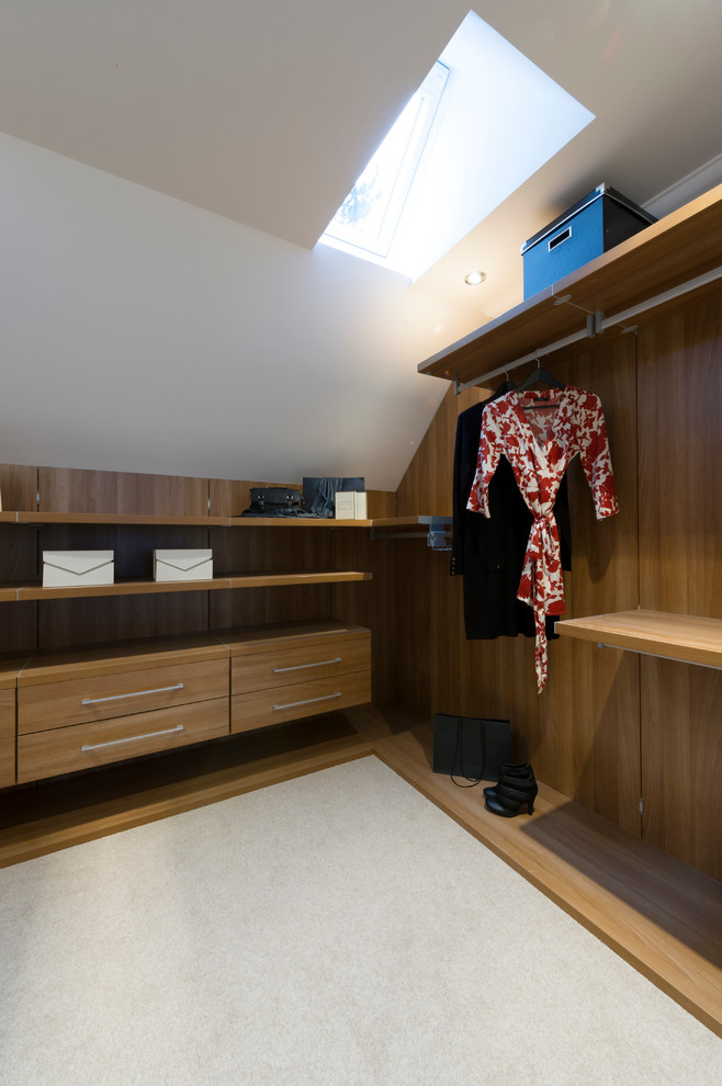 Ejemplo de vestidor unisex actual de tamaño medio con armarios con paneles lisos, puertas de armario de madera oscura y moqueta