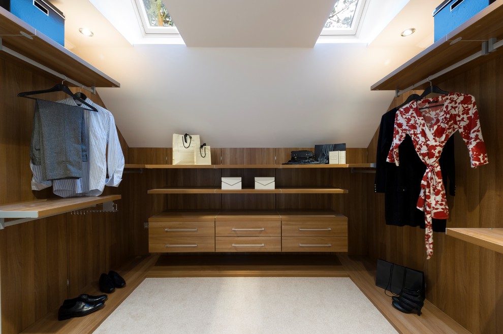 This is an example of a medium sized contemporary gender neutral dressing room in West Midlands with flat-panel cabinets, medium wood cabinets and carpet.