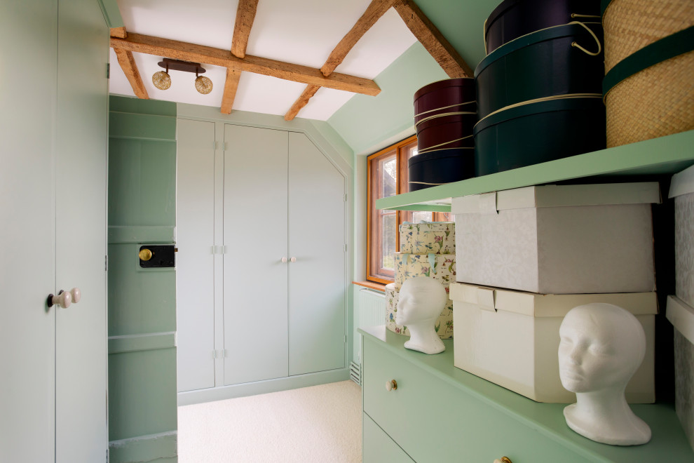Landhaus Begehbarer Kleiderschrank mit flächenbündigen Schrankfronten, grünen Schränken, Teppichboden, beigem Boden und freigelegten Dachbalken in Kent
