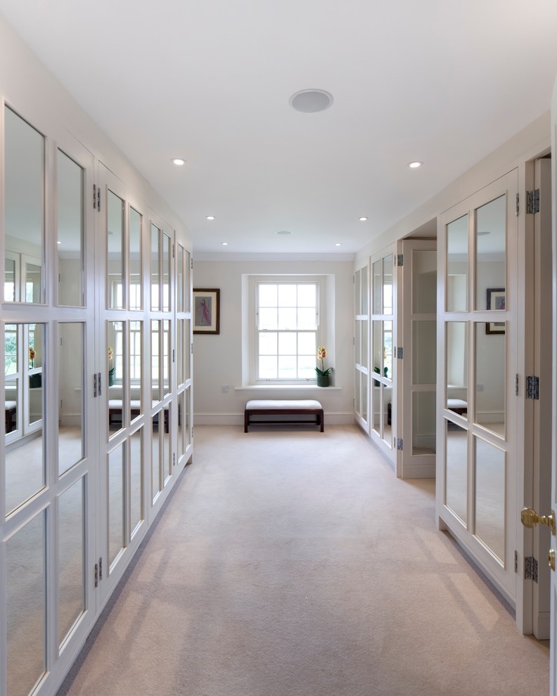 Пример оригинального дизайна: гардеробная комната унисекс в стиле неоклассика (современная классика) с стеклянными фасадами, белыми фасадами и ковровым покрытием