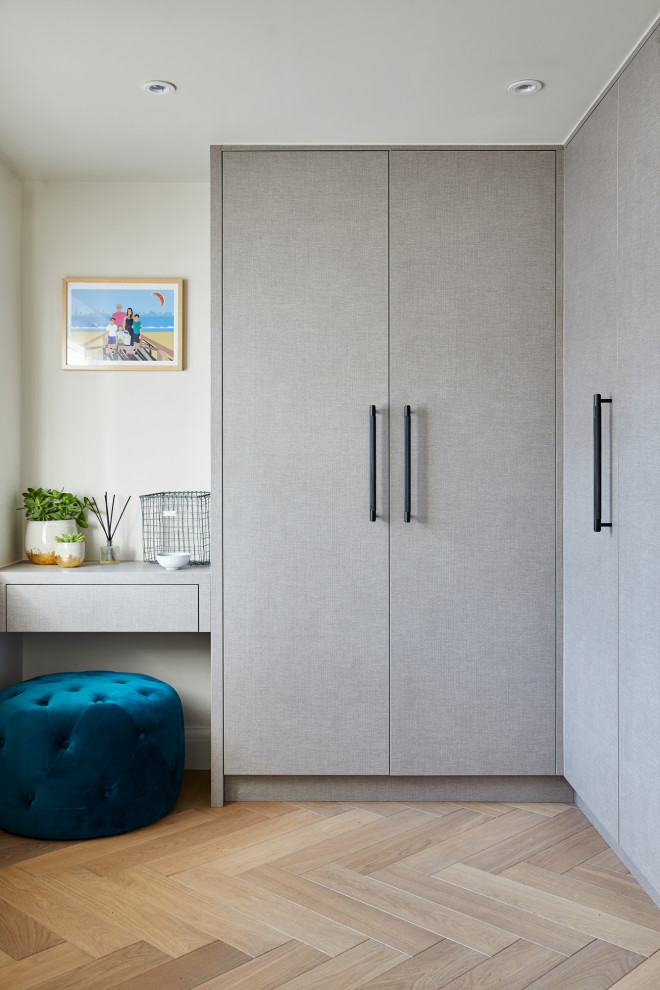 Photo of a contemporary dressing room in Surrey with flat-panel cabinets, grey cabinets, light hardwood flooring and beige floors.
