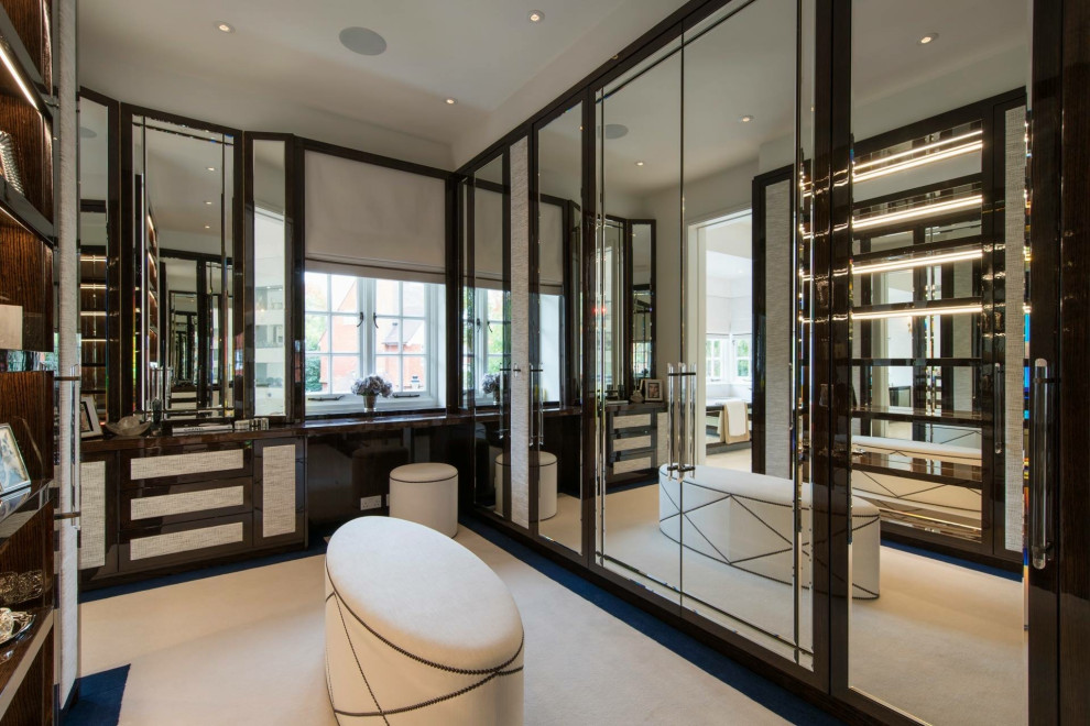 Inspiration for a large modern gender neutral walk-in wardrobe in London with glass-front cabinets, brown cabinets, carpet and beige floors.