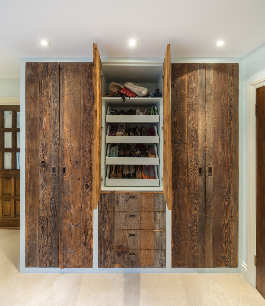 Ejemplo de armario unisex clásico de tamaño medio con armarios con paneles lisos, puertas de armario de madera oscura, moqueta y suelo beige
