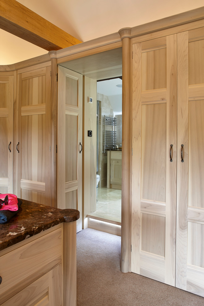 This is an example of an expansive modern gender neutral dressing room in Surrey with recessed-panel cabinets, light wood cabinets and carpet.
