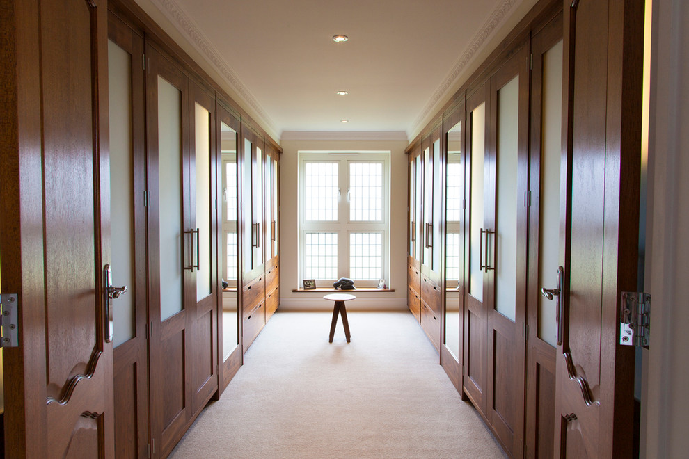 На фото: большая гардеробная комната унисекс в классическом стиле с фасадами с утопленной филенкой, фасадами цвета дерева среднего тона и ковровым покрытием