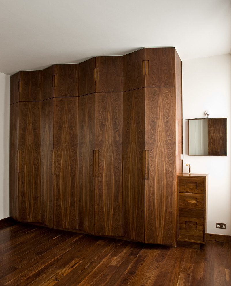 Large contemporary gender neutral standard wardrobe in London with flat-panel cabinets, dark wood cabinets and dark hardwood flooring.