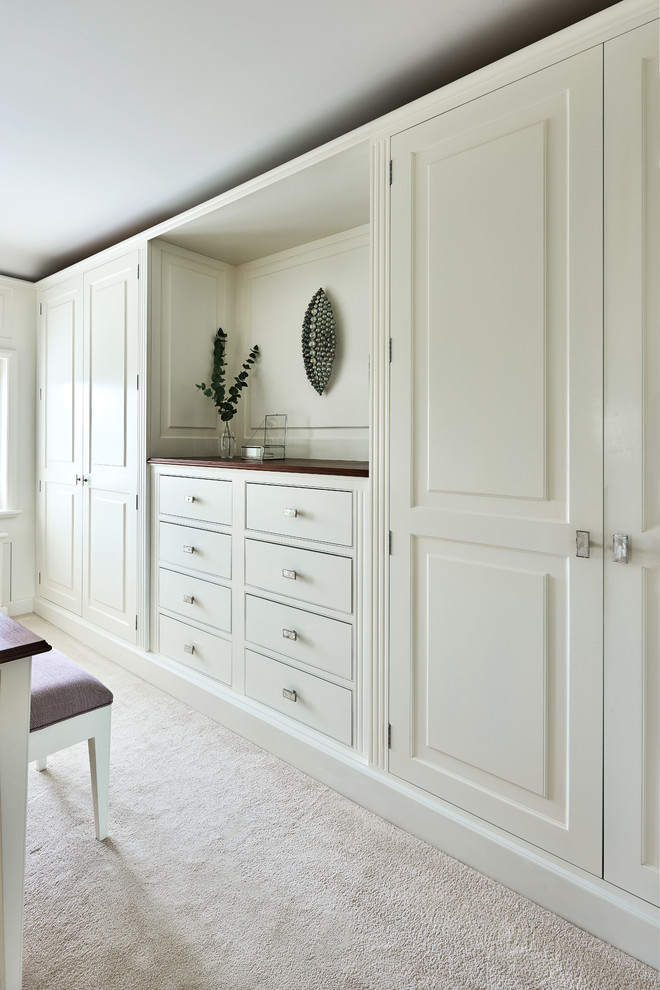 Cette photo montre un dressing room nature de taille moyenne avec un placard avec porte à panneau surélevé, des portes de placard blanches et moquette.