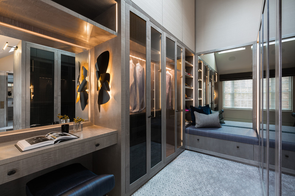 Photo of a contemporary gender neutral dressing room in London with glass-front cabinets, medium wood cabinets, carpet and grey floors.