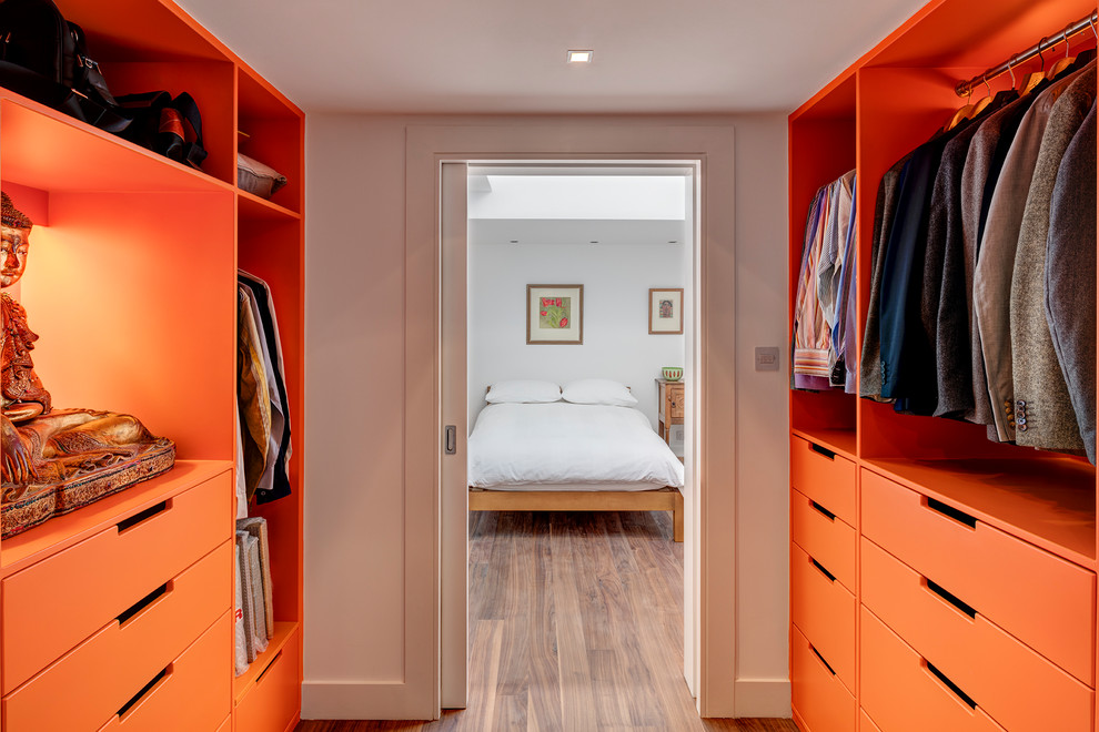 Diseño de armario vestidor unisex actual con armarios con paneles lisos, puertas de armario naranjas, suelo de madera oscura y suelo marrón